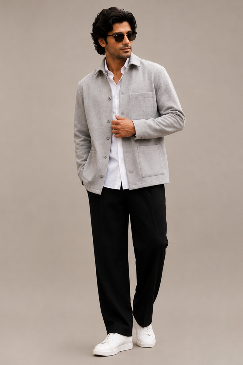 Indian male model wearing a light grey shacket layered over a white shirt, styled with black trousers, white sneakers, and sunglasses against a beige studio background.