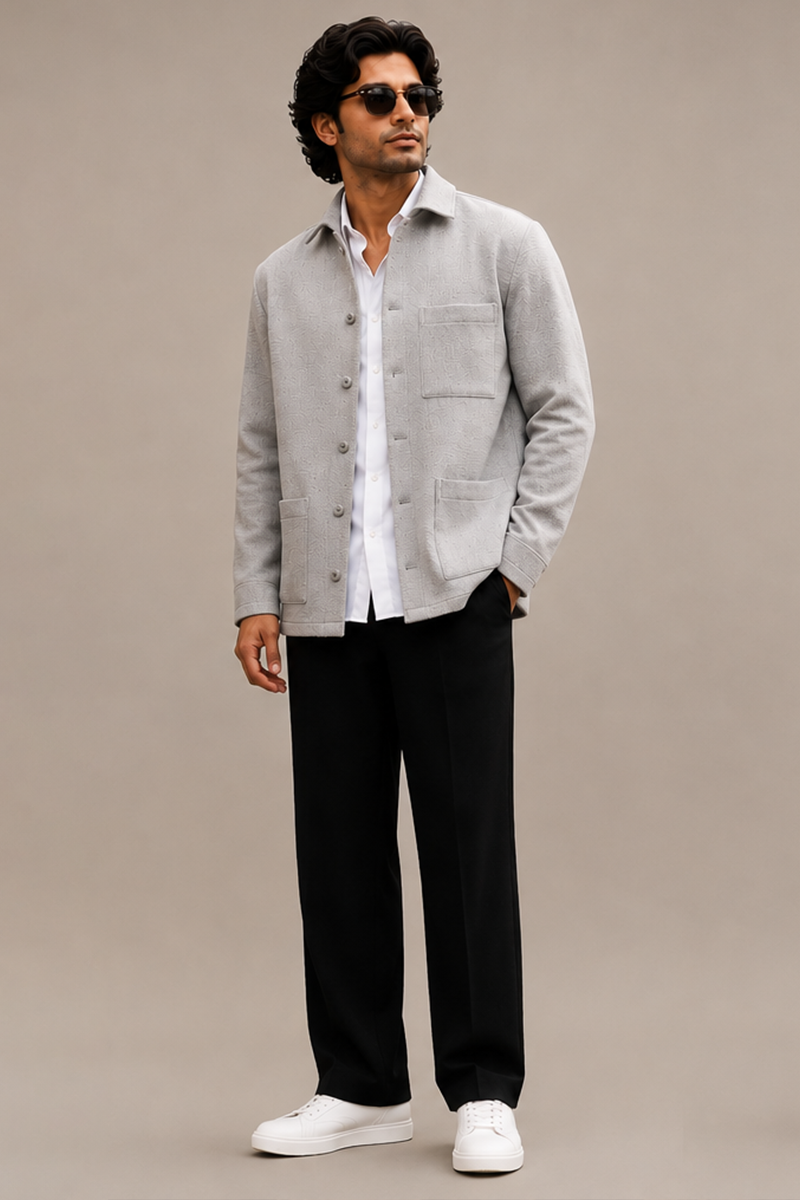 Indian male model wearing a light grey shacket over a white shirt, paired with black trousers, white sneakers, and sunglasses against a beige studio background.
