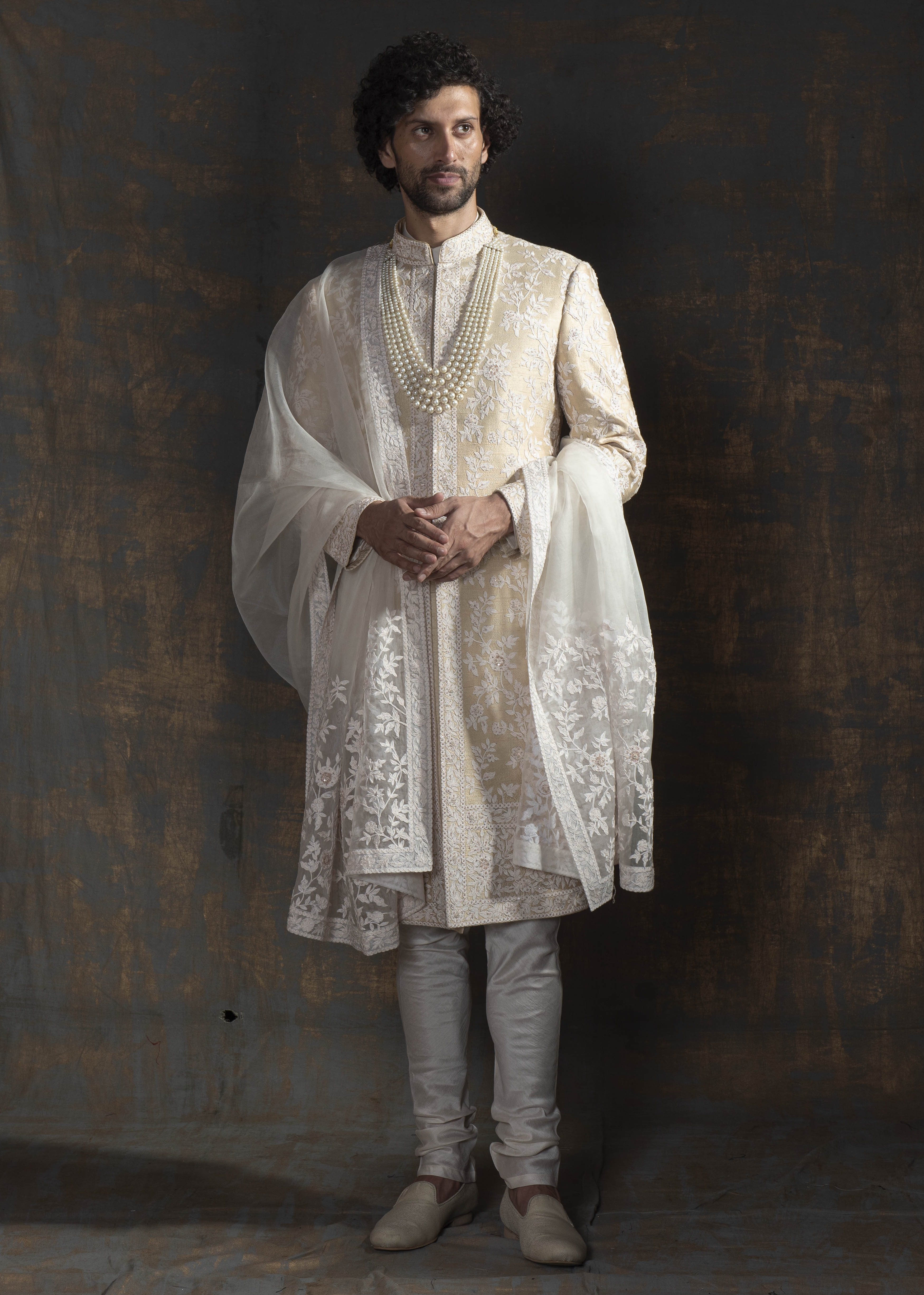 Champagne coloured raw silk sherwani with ivory thread embroidery all over.  Paired up with off white kurta pajama and a stole made in organza with the sherwani's embroidery on it.