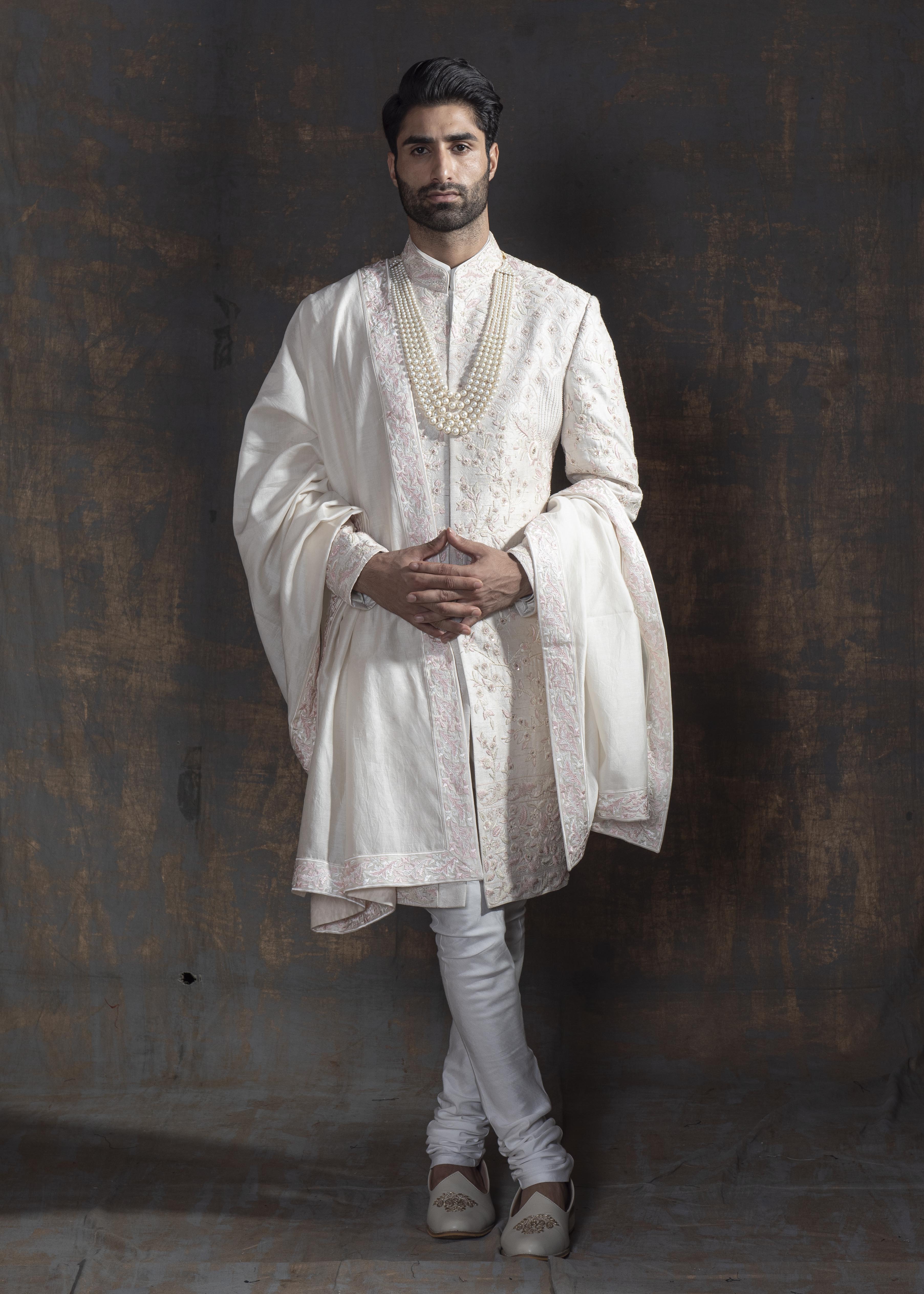 Ivory raw silk sherwani with all over light pink coloured hand embroidery. Paired up with off white kurta and chooridaar and an ivory stole with the sherwani's embroidery as the border.