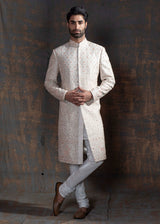 Ivory raw silk sherwani with all over light peach coloured hand embroidery.  Paired up with off white kurta and chooridaar and an ivory stole with the sherwani's embroidery as the border.