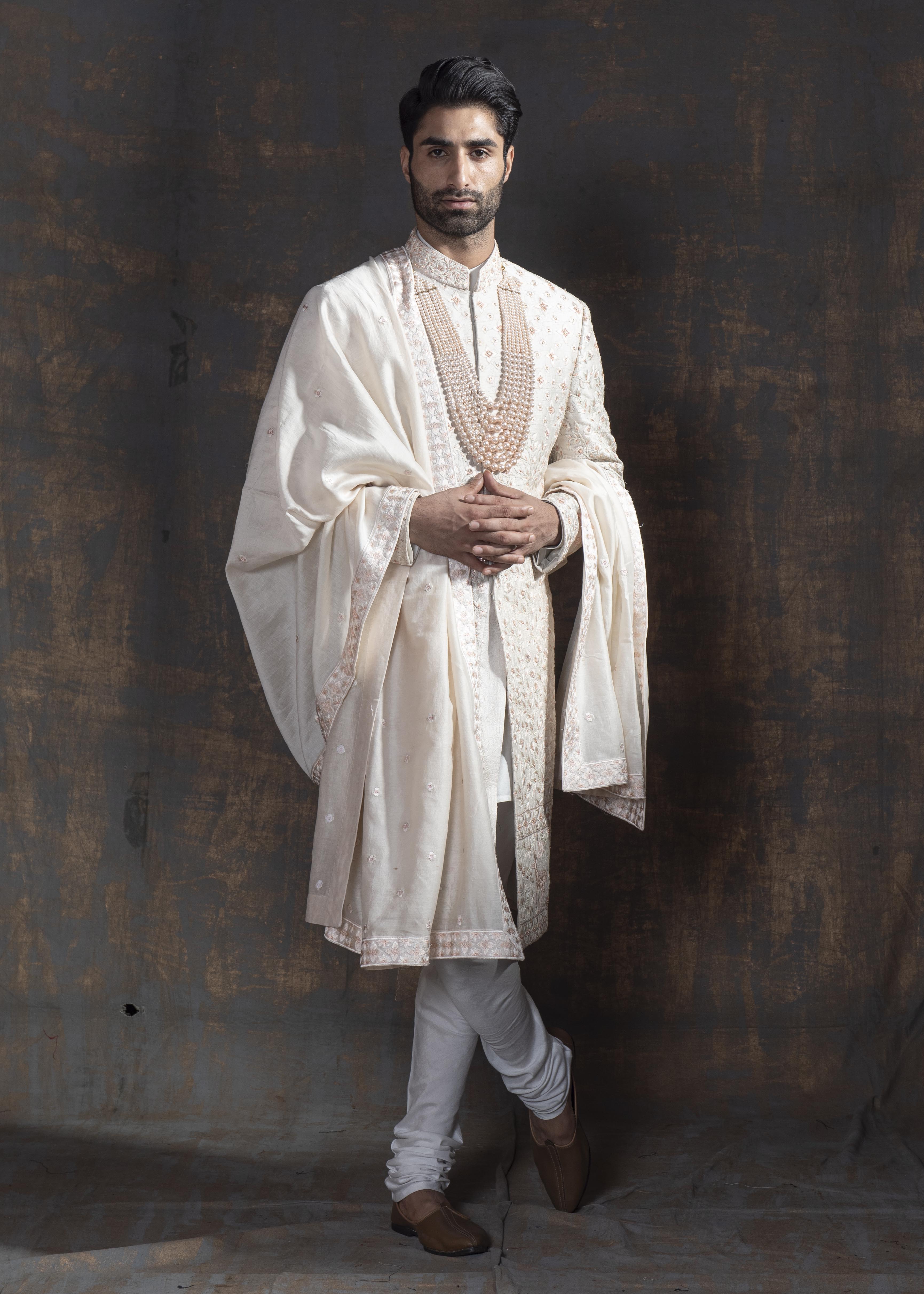 Ivory raw silk sherwani with all over light peach coloured hand embroidery.  Paired up with off white kurta and chooridaar and an ivory stole with the sherwani's embroidery as the border.