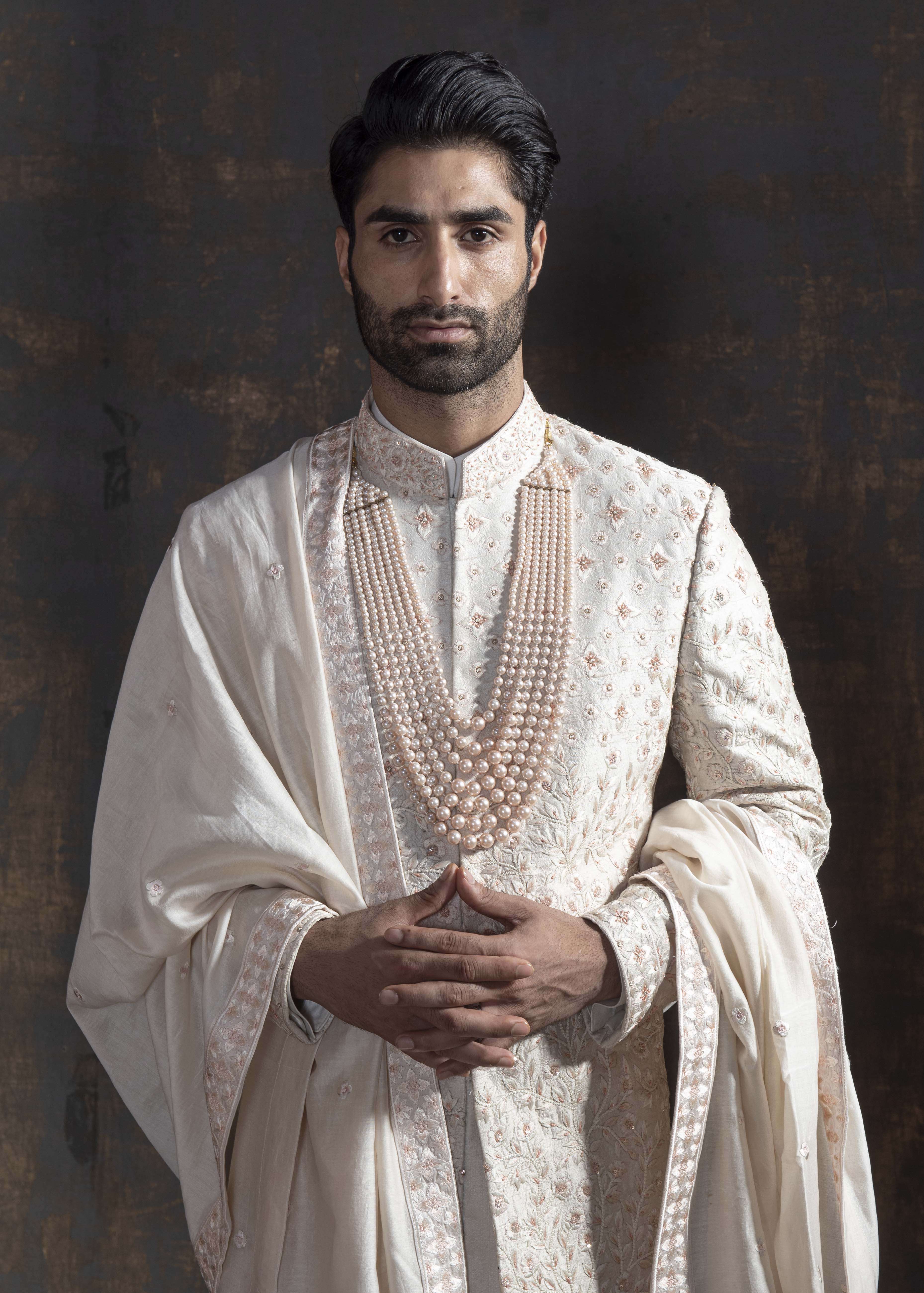 Ivory raw silk sherwani with all over light peach coloured hand embroidery.  Paired up with off white kurta and chooridaar and an ivory stole with the sherwani's embroidery as the border.