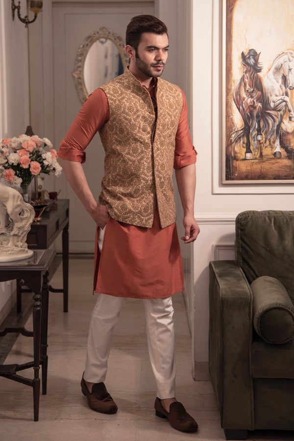 Gold heavy embroidered nehru jacket with rust coloured kurta and off white pajama.