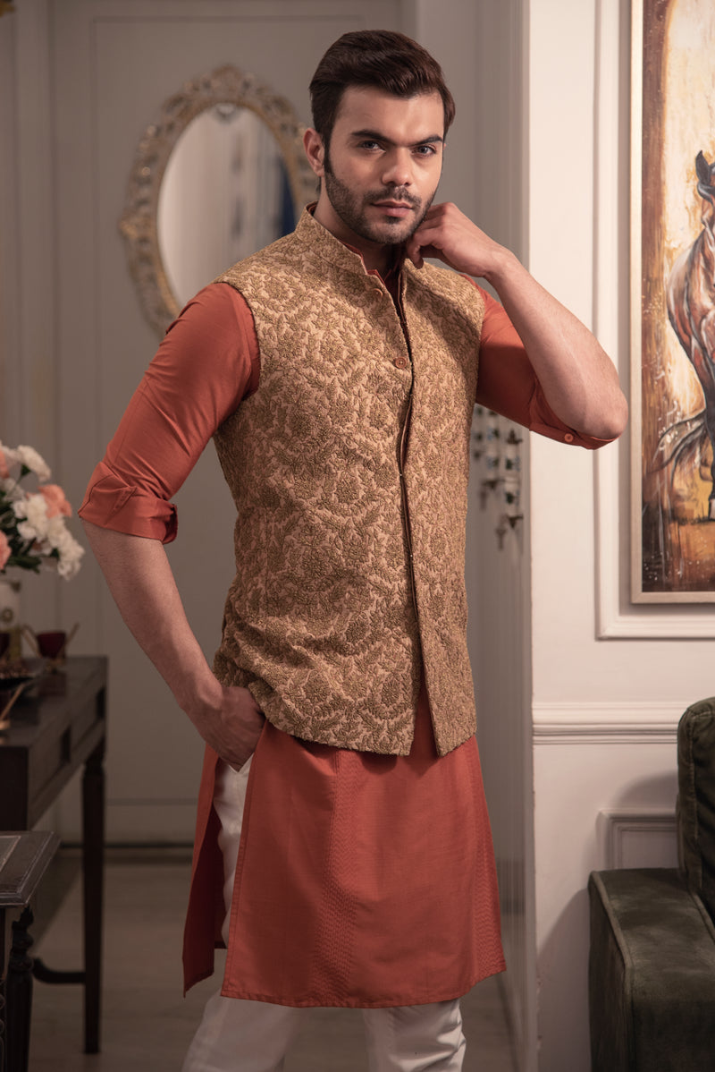Gold heavy embroidered nehru jacket with rust coloured kurta and off white pajama.