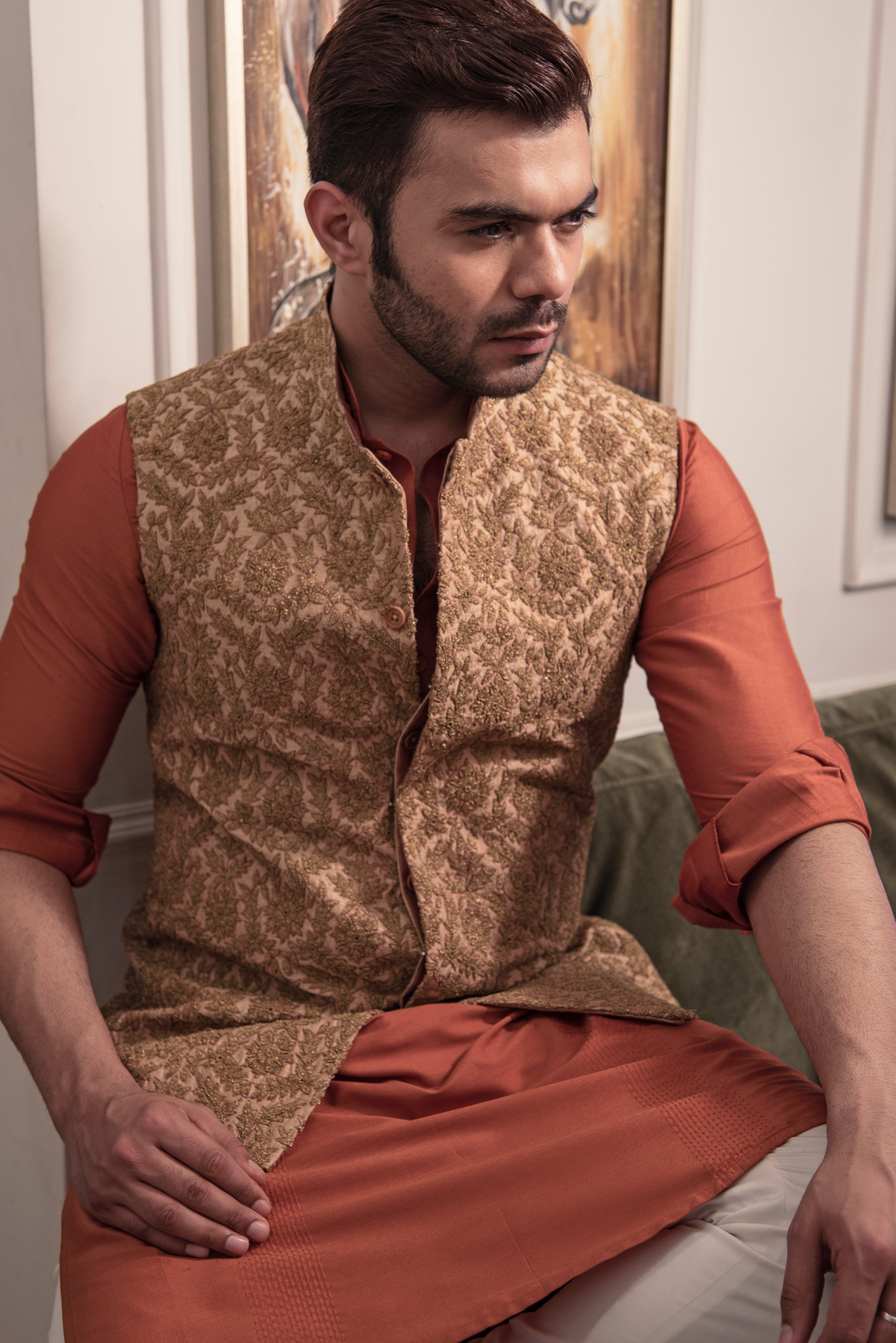 Gold heavy embroidered nehru jacket with rust coloured kurta and off white pajama.